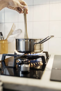 Cropped image of woman's hand holding spatula in sauce pan while cooking food on stove