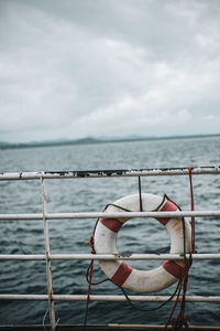 Life belt hanging on railing over sea against cloudy sky