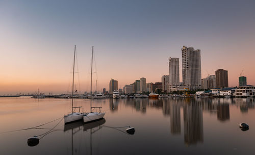 Sailboats moored in city against sky during sunset