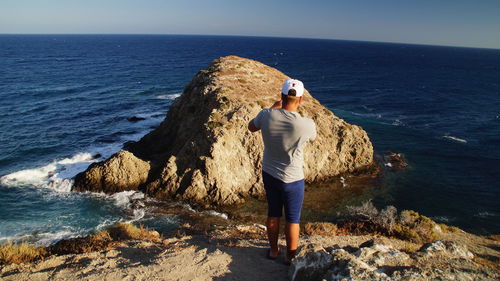 Rear view of man standing on rock by sea