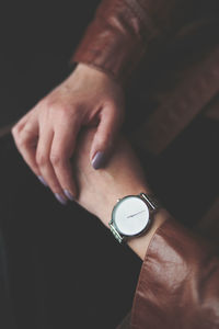 Midsection of woman wearing leather jacket and wristwatch while standing against blue wall