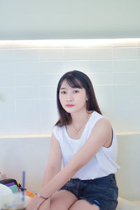 Portrait of young woman sitting against wall