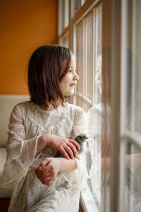 A happy girl gazes out the window, a baby chick nestled in her arms