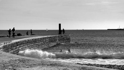 People walking on jetty against calm sea