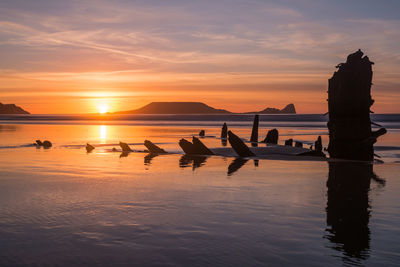 Silhouette people on beach against sky during sunset