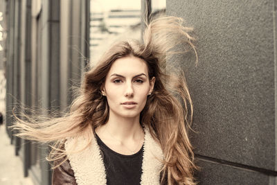 Portrait of beautiful young woman with tousled hair against wall