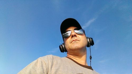 Low angle view of man listening music against blue sky