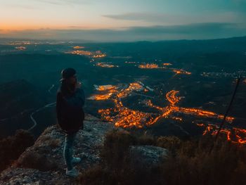 High angle view of woman standing on cliff against illuminated city at night