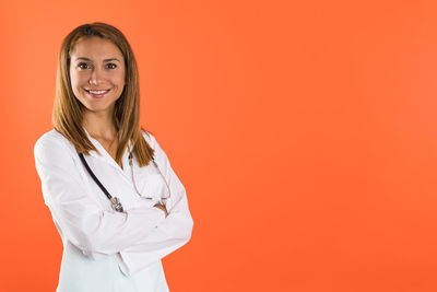 Portrait of female doctor standing against yellow background