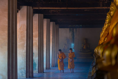 Full length of boys wearing traditional clothing walking on floor in buddhist temple