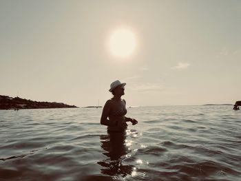 Side view of man in sea against sky during sunset