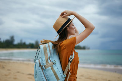 Young woman standing at beach against sky