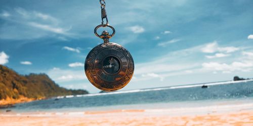 Close-up of pocket watch on beach against sky