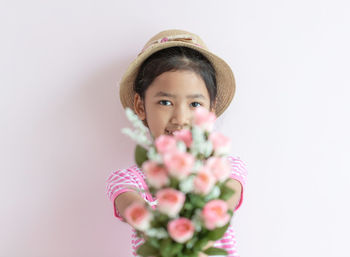 Portrait of girl holding pink flower against white background