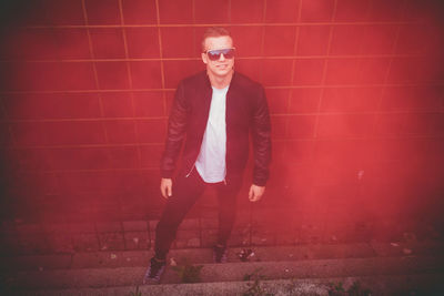 Portrait of young man wearing sunglasses standing against red wall