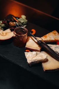 Composition of sliced cheese, a jar of honey and pieces of apples on a wooden stand