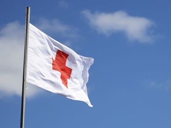 Low angle view of red cross flag against blue sky