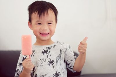 Portrait of smiling boy with popsicle showing thumbs up sign