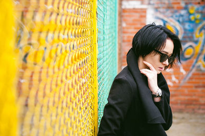 Young woman in sunglasses standing against chainlink fence