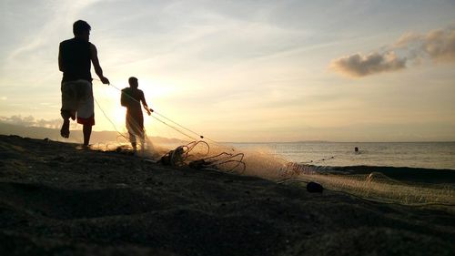 Fishermen with net at beach against sky during sunset