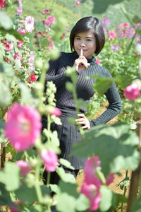 Portrait of woman with finger on lips standing by flowering plants