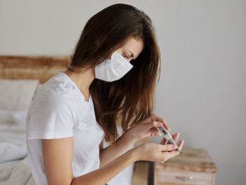 Young woman looking away while standing against white wall