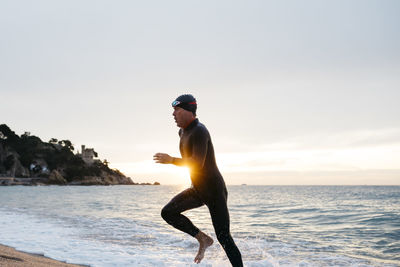 Male swimmer leaving water after swimming in sea at sunset