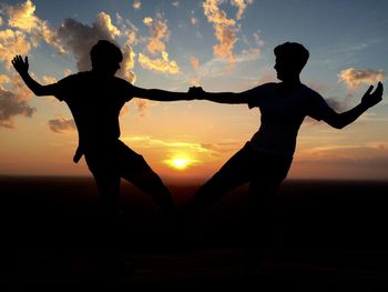 Silhouette men on beach against sky during sunset
