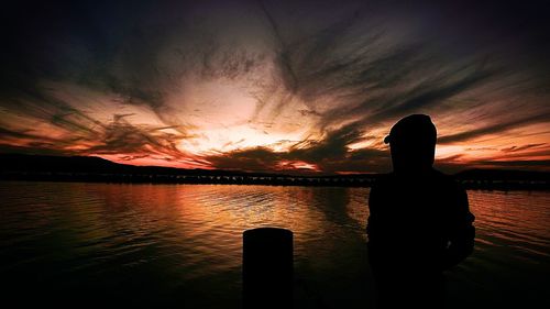 Silhouette man sitting by lake against sky during sunset