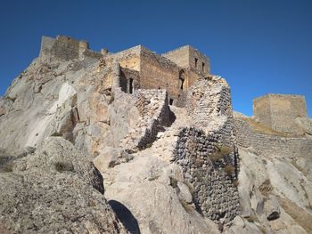 Low angle view of rocks on mountain against blue sky