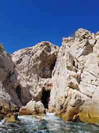 Rock formations by sea against clear blue sky