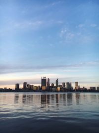 River by city buildings against sky during sunset