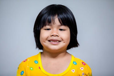 Close-up portrait of smiling cute girl against gray background