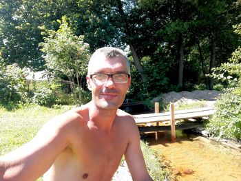 Portrait of shirtless man wearing sunglasses against trees