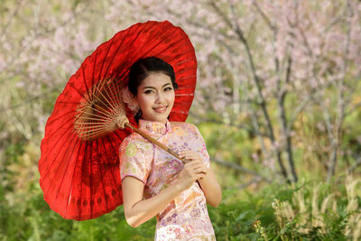 Portrait of smiling young woman with umbrella standing on field