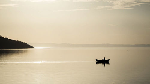 Silhouette man in sea against sky during sunset