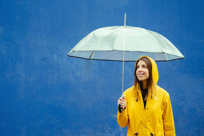 Portrait of young woman holding umbrella against blue background