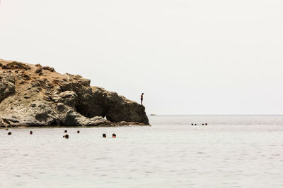 Man standing on rock formation by sea against clear sky during sunny day