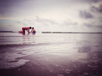 Boys playing on shore at beach against sky