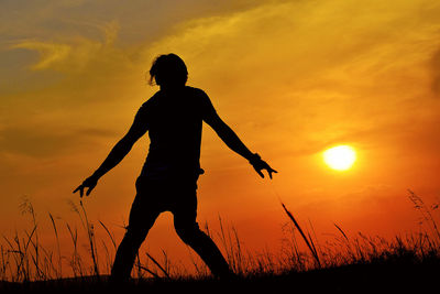 Silhouette woman dancing on land against sky during sunset