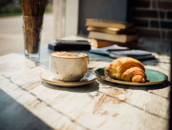 Cappuccino and croissant are lying on the table in a cafe against the background of a window.