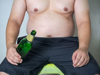 Midsection of shirtless man sitting in beer bottle