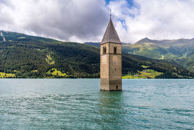 Tower by lake and buildings against sky
