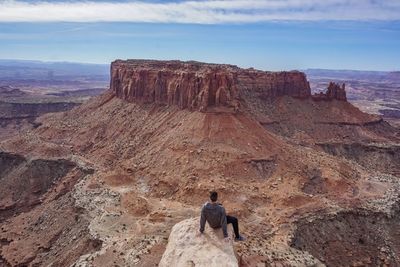 High angle view of man sitting on cliff against blue sky