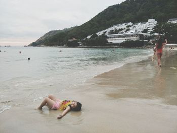 Girl lying on shore at beach against mountain