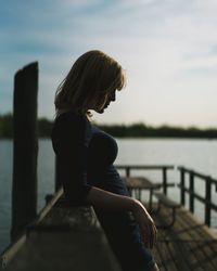 Rear view of woman sitting by sea against sky