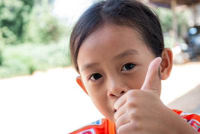 Close-up portrait of cute girl gesturing thumbs up outdoors