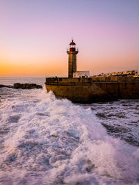 Lighthouse by sea against sky during sunset