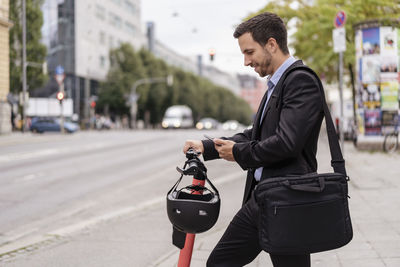 Businessman with e-scooter using cell phone in the city