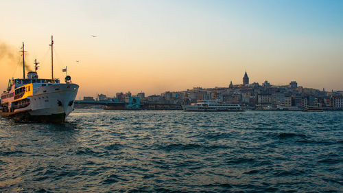 Ship in sea by buildings against sky during sunset